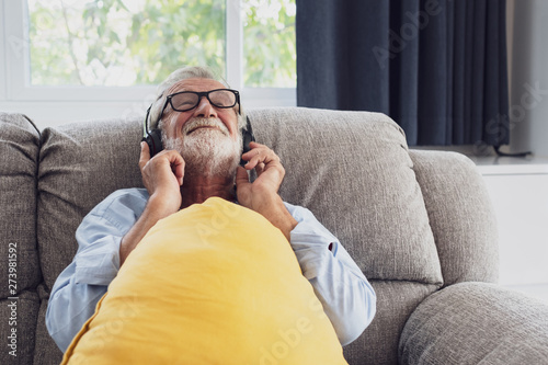 senior man happiness sitting on the sofa and listening music with headphone at living room for relaxing