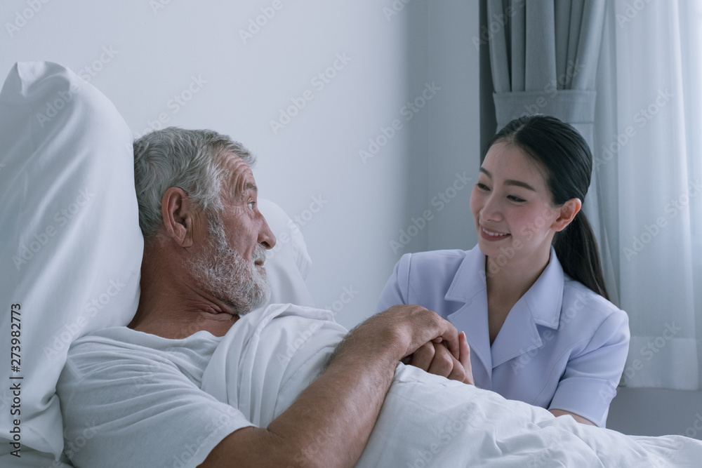 Obraz premium senior man with smiling nurse, takes care and discussion and cheer on bed at nursing home
