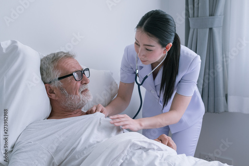senior man with smiling nurse  takes care and discussion after health check by stethoscope and cheer on bed at nursing home