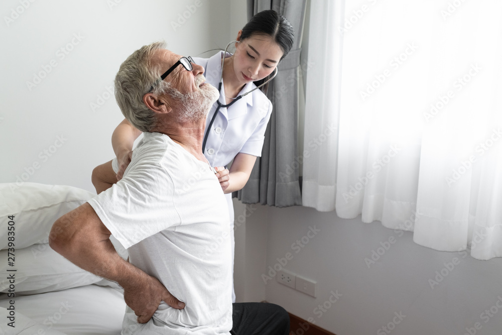 Obraz premium senior man back ache with smiling nurse, takes care and discussion on bed at nursing home