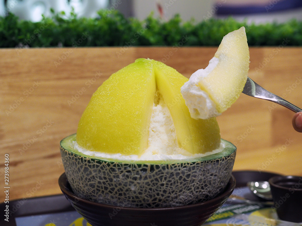 Whole melon shaved ice, also known as Bingsu Korean dessert, served with whipped cream and sweetened condensed milk on the wooden table. It's very popular dessert. Whole melon shaved ice, also known as Bingsu Korean dessert, served with whipped cream and sweetened condensed milk on the wooden table. It's very popular dessert.