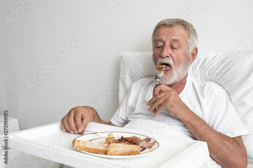 senior man with smiling nurse, takes care breakfast and discussion and cheer on bed at nursing home
