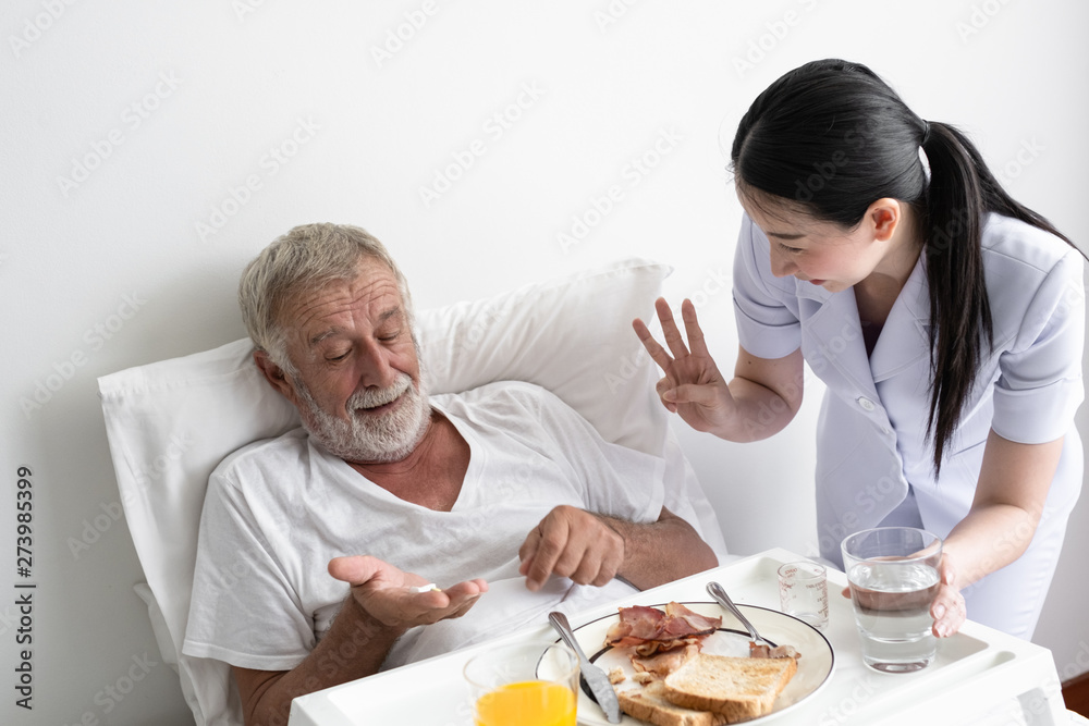 nurse give pill to senior man after breakfast and discussion on bed at nursing home nurse give pill to senior man after breakfast and discussion on bed at nursing home