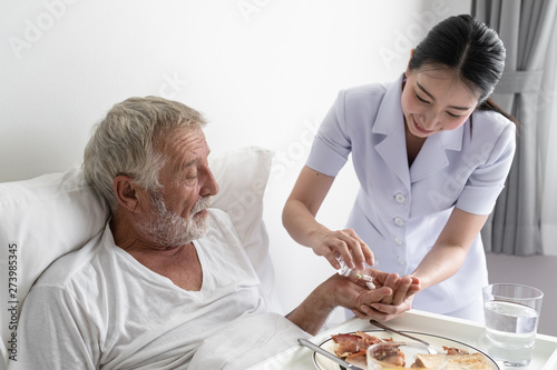 nurse give pill to senior man after breakfast and discussion on bed at nursing home