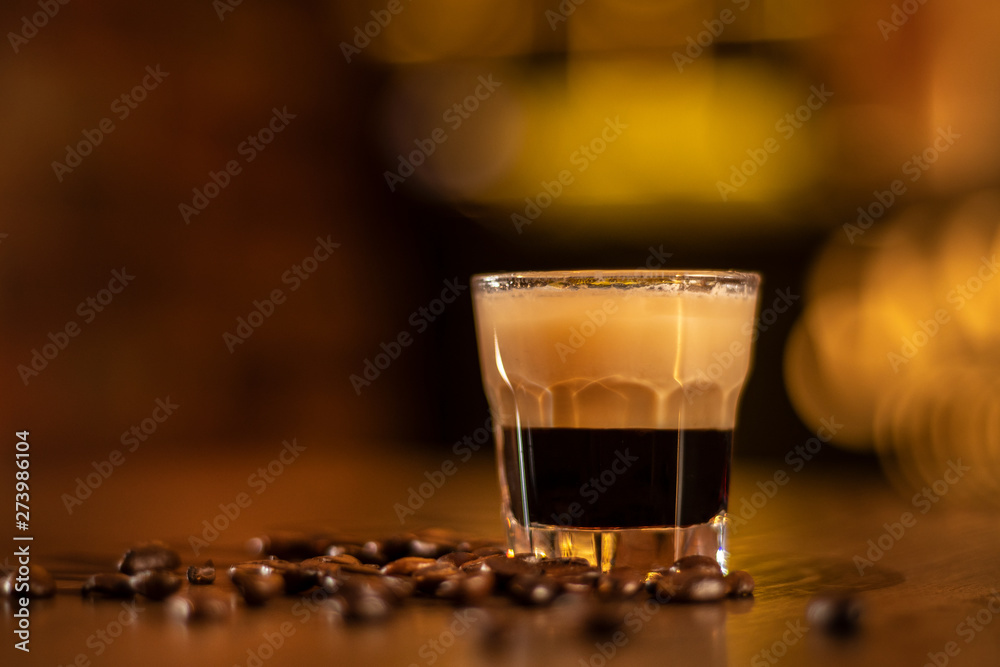 shot with coffee in the glass and coffee beans on wooden table in bar