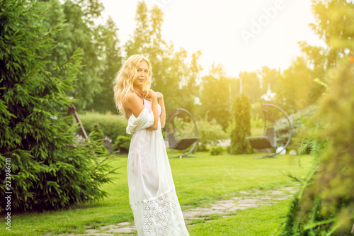 Youmg beautiful blond woman in beautiful summer garden is barefoot on lawn
