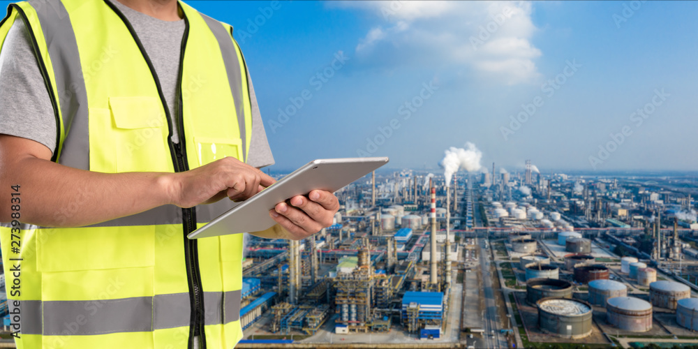worker working on pad with oil and gas refinery background,Smart factory concept.