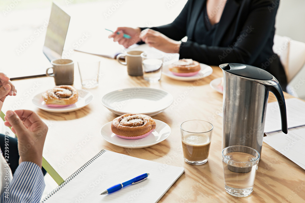People in a meeting with cinnamon buns on the table People in a meeting with cinnamon buns on the table