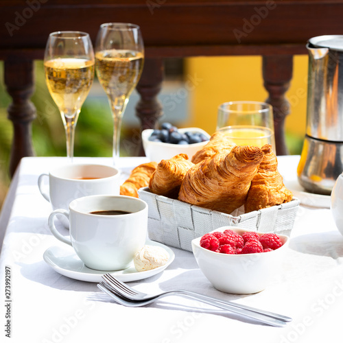 Luxury brunch on the hotel terrace, coffee maker, teapot, cups, croissants, fruits, orange juice and champagne. Good morning scenery background.