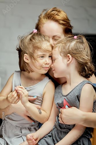 Two little beautiful twin girls with mum cuddle at home.