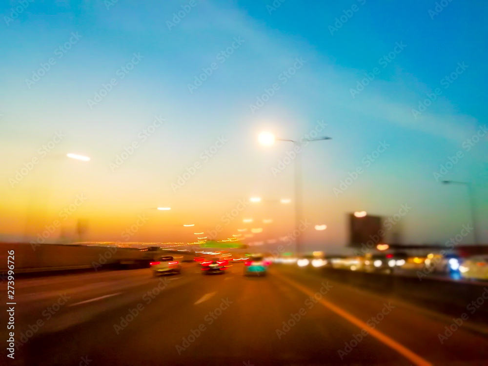 On the expressway, there are colorful lights and evening sky. With lots of cars and trucks.