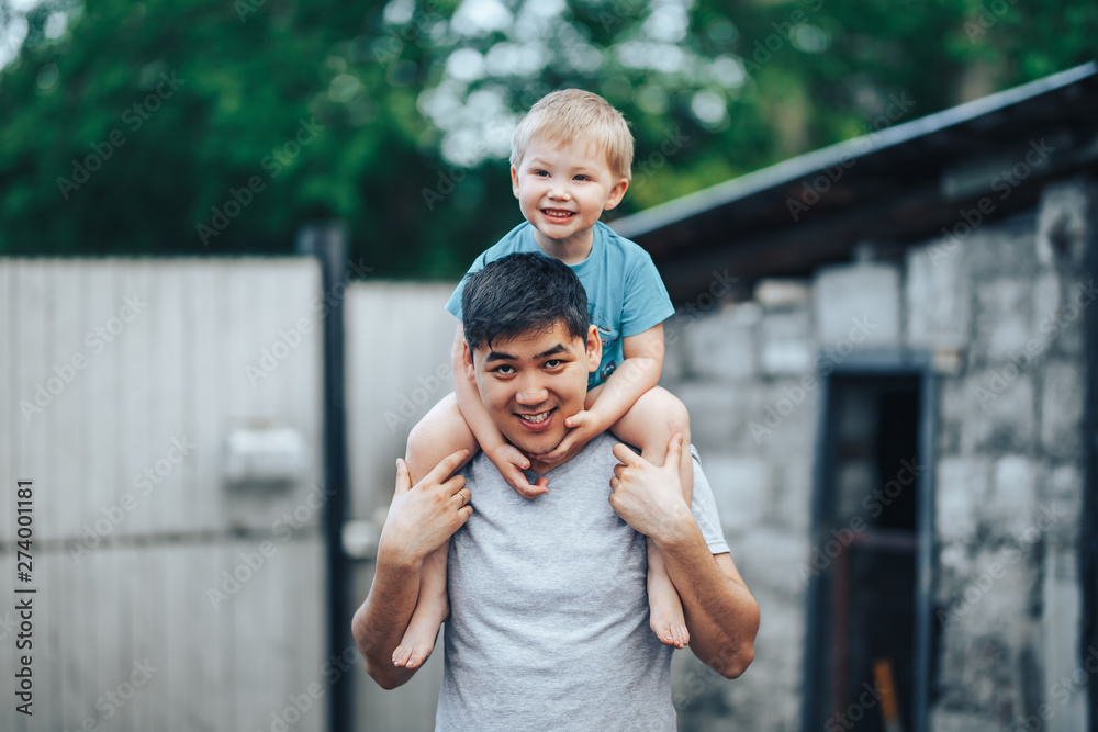 blonde three years old boy sitting on father's shoulders. Kazakh father and  caucasian mother. Happy father with black hair play with his caucasian son  Stock Photo | Adobe Stock