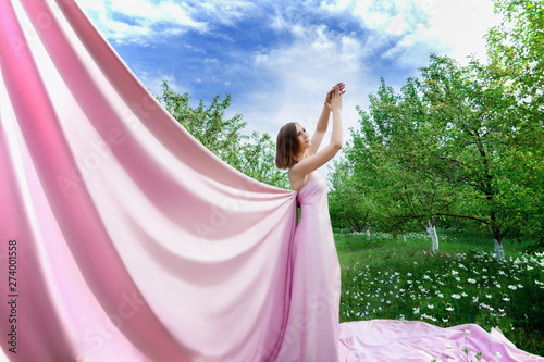magical photo of a girl in a long rose fabric on the background of a beautiful summer forest