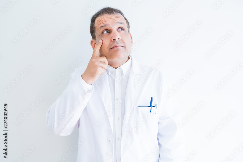 Middle age doctor man wearing medical coat over white background with hand on chin thinking about question, pensive expression. Smiling with thoughtful face. Doubt concept. Middle age doctor man wearing medical coat over white background with hand on chin thinking about question, pensive expression. Smiling with thoughtful face. Doubt concept.