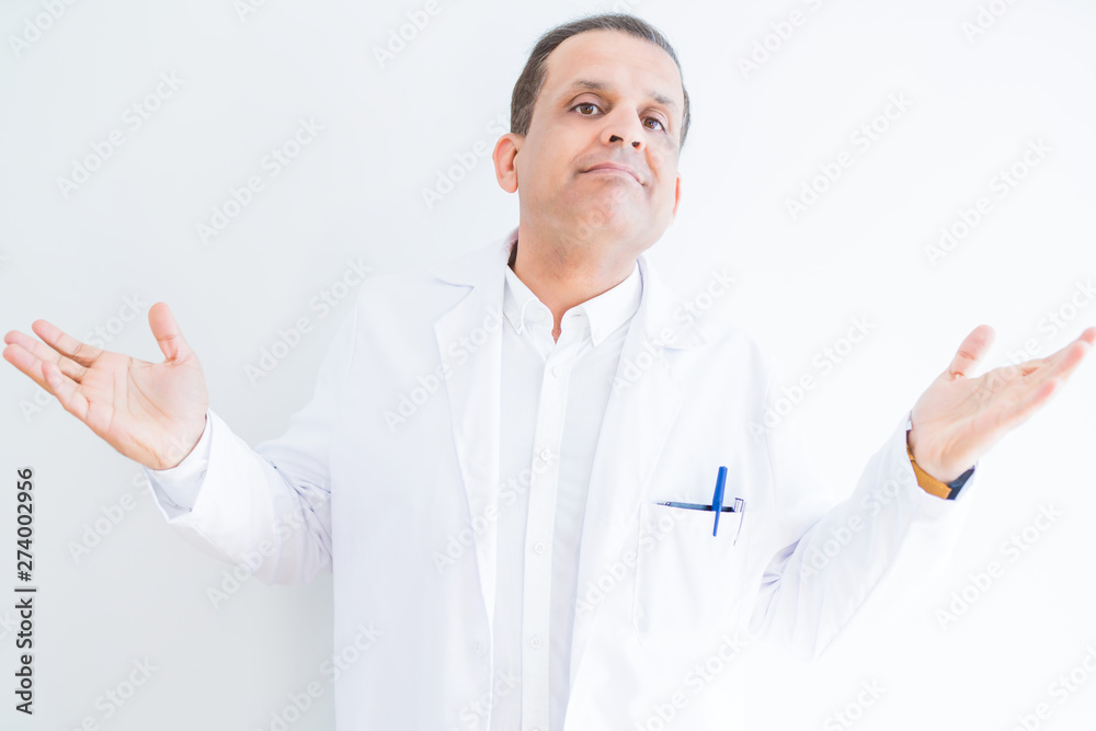 Middle age doctor man wearing medical coat over white background clueless and confused expression with arms and hands raised. Doubt concept. Middle age doctor man wearing medical coat over white background clueless and confused expression with arms and hands raised. Doubt concept.
