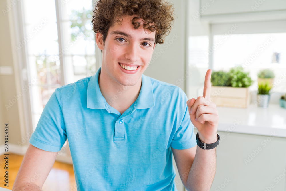 Young handsome man wearing casual blue t-shirt at home pointing finger up with successful idea. Exited and happy. Number one. Young handsome man wearing casual blue t-shirt at home pointing finger up with successful idea. Exited and happy. Number one.
