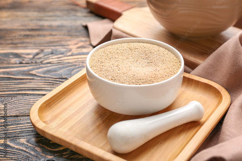 Bowl with white poppy seeds and pestle on wooden background