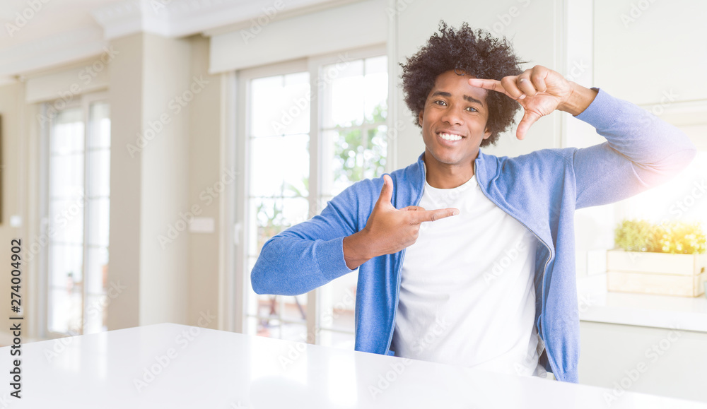 African American man at home smiling making frame with hands and fingers with happy face. Creativity and photography concept.