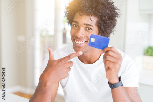African American man holding credit card very happy pointing with hand and finger