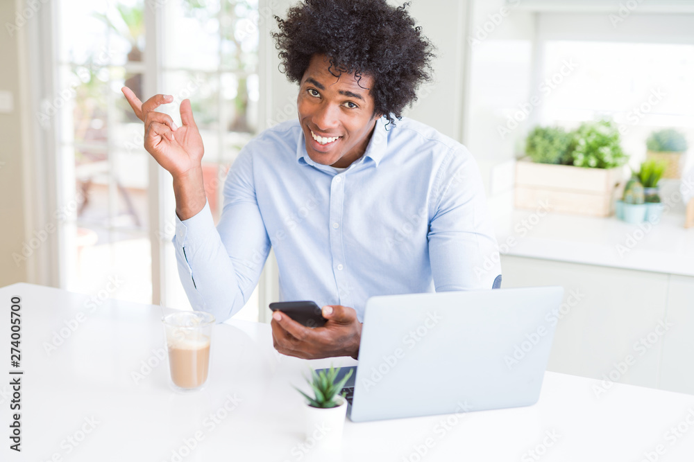 African American business man using smartphone and laptop very happy pointing with hand and finger to the side African American business man using smartphone and laptop very happy pointing with hand and finger to the side