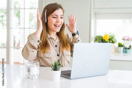 Beautiful young operator woman working with laptop and wearing headseat very happy and excited, winner expression celebrating victory screaming with big smile and raised hands