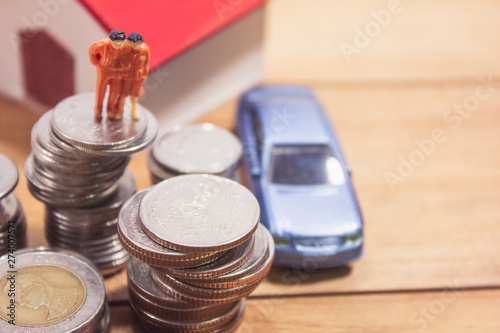 Miniature family stand with coins house and car on wooden table. family planning concept.