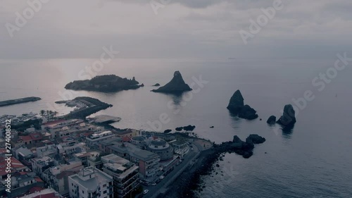 Aerial orbiting view of the fishing village of Acitrezza in East Sicily and the Faraglioni, basalt formations in the sea photo