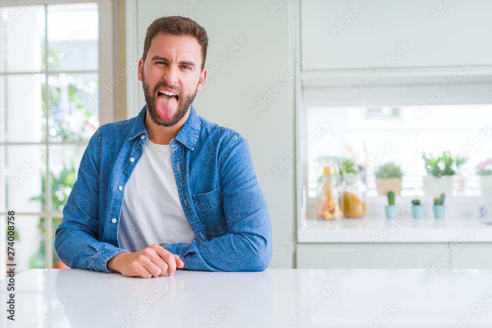 Handsome man at home sticking tongue out happy with funny expression. Emotion concept.