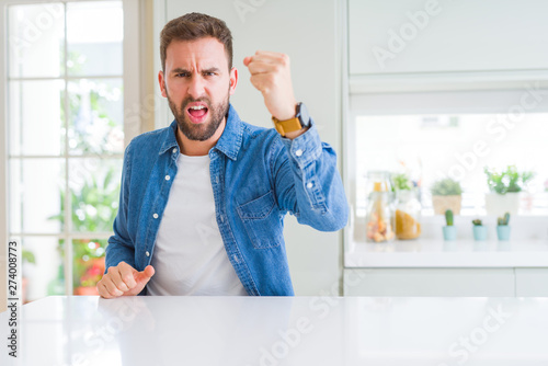 Handsome man at home angry and mad raising fist frustrated and furious while shouting with anger. Rage and aggressive concept.