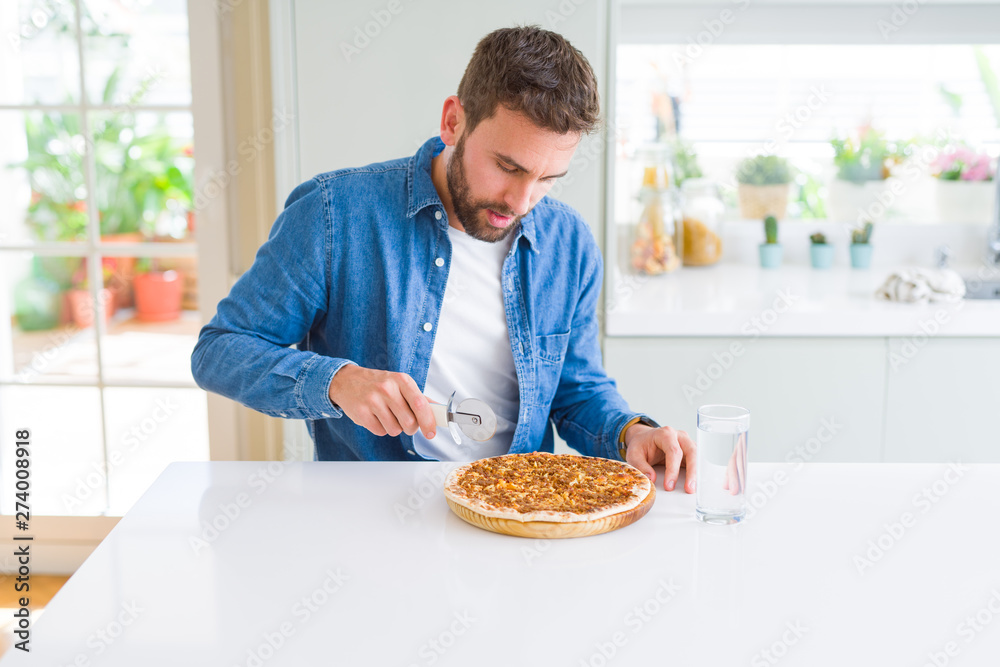 Handsome man cutting a pizza slice at home Handsome man cutting a pizza slice at home