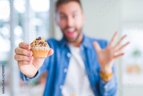Handsome man eating chocolate chips muffin very happy and excited  winner expression celebrating victory screaming with big smile and raised hands
