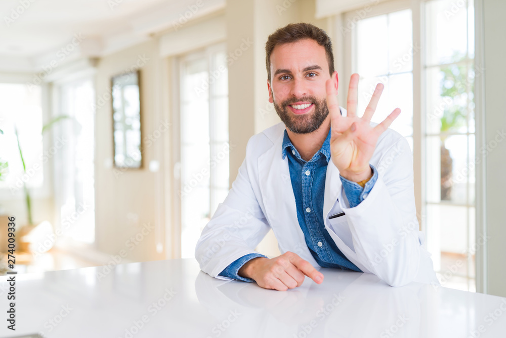 Handsome doctor man wearing medical coat at the clinic showing and pointing up with fingers number four while smiling confident and happy.