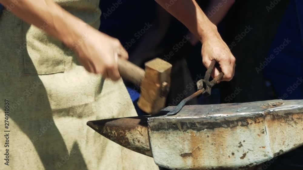 A Blacksmith Holding a Massive Hammer Banging Hot Metal Bar on Anvil. A Blacksmith Holding a Massive Hammer Banging Hot Metal Bar on Anvil.
