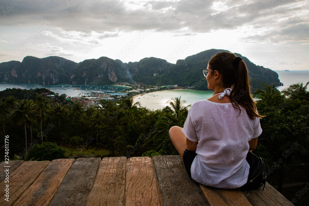 Beautiful woman sitting on wooden platform with Phi Phi island views and cloudy sky