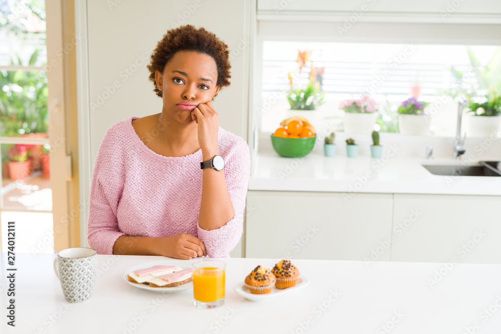 Young african american woman eating breaksfast in the morning at home thinking looking tired and bored with depression problems with crossed arms. Young african american woman eating breaksfast in the morning at home thinking looking tired and bored with depression problems with crossed arms.