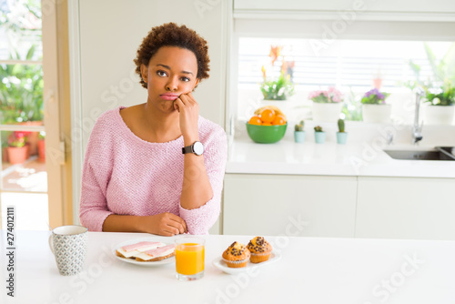 Young african american woman eating breaksfast in the morning at home thinking looking tired and bored with depression problems with crossed arms.