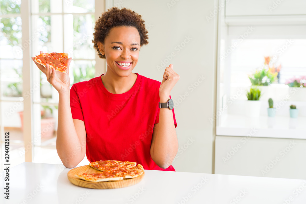 Young african american woman eating tasty peperoni pizza screaming proud and celebrating victory and success very excited, cheering emotion Young african american woman eating tasty peperoni pizza screaming proud and celebrating victory and success very excited, cheering emotion