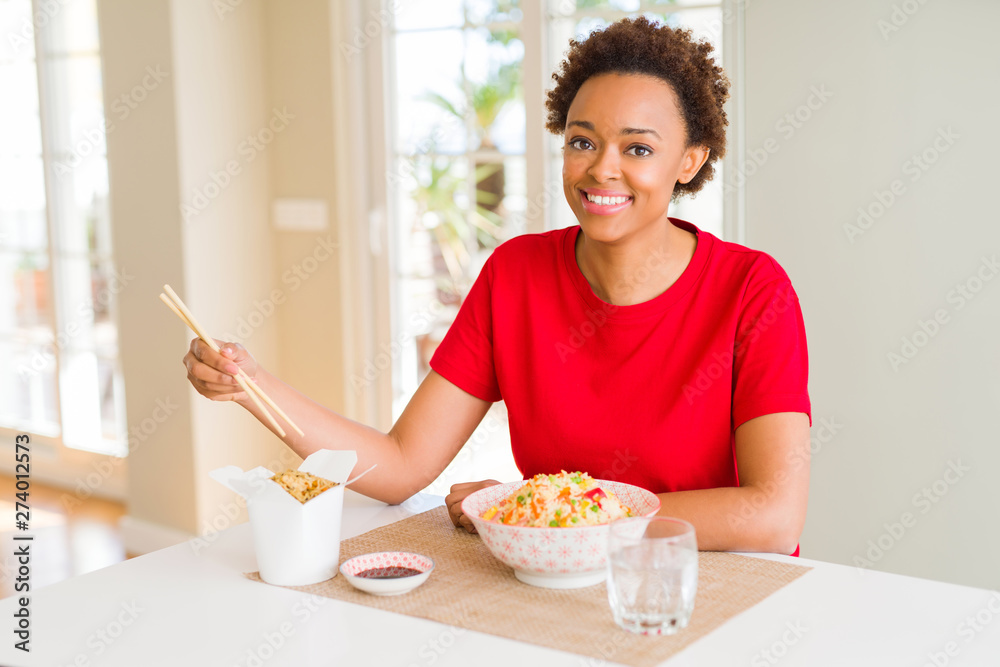 Young african american woman with afro hair eating asian food at home with a happy face standing and smiling with a confident smile showing teeth Young african american woman with afro hair eating asian food at home with a happy face standing and smiling with a confident smile showing teeth