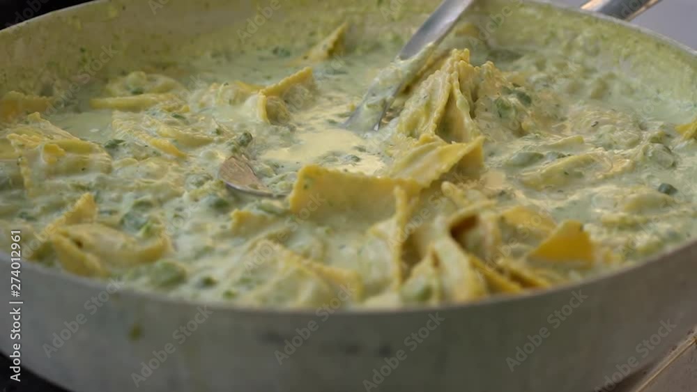 Simmering ravioli with white sauce getting cooked in a huge pan and stirred - close up shot Simmering ravioli with white sauce getting cooked in a huge pan and stirred - close up shot