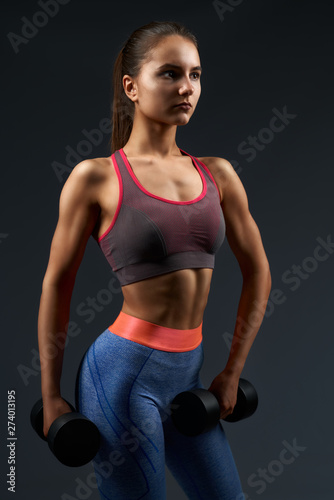 Athletic brunette woman pumping biceps with dumbbells