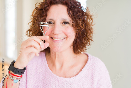 Senior woman using eyelashes curler and mascara with a happy face standing and smiling with a confident smile showing teeth