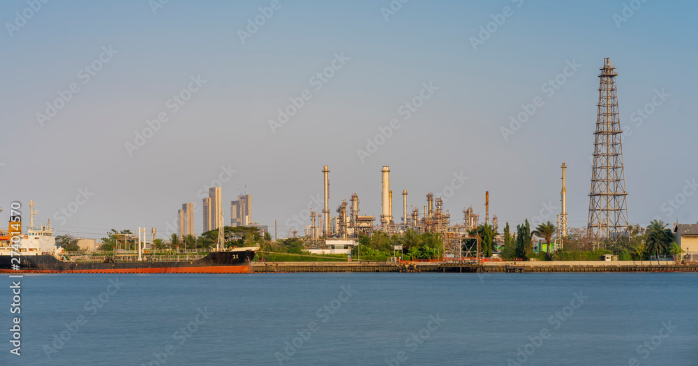 Crude oil refinery plant and many chimney with petrochemical tanker or cargo ship at coast of river on sky afternoon  bright day at thailand