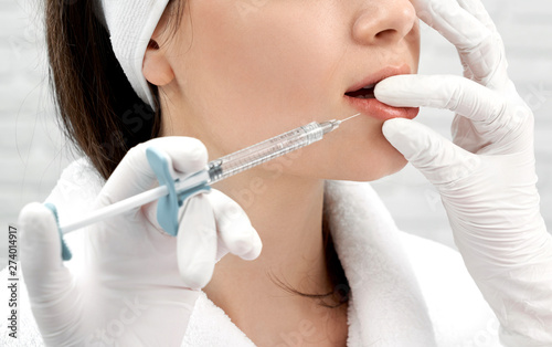 Cosmetologist plumping lower lip with collagen in salon photo