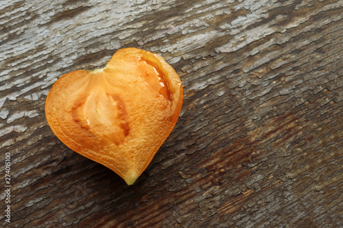 half a orange tomato in the shape of a heart lies on a grungy wooden background with copy space. organic fruits and vegetables have a positive effect on human health.
