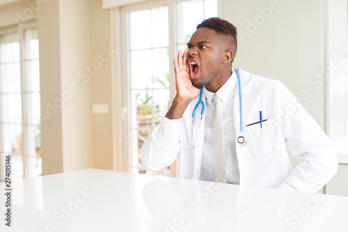African american doctor man at the clinic shouting and screaming loud to side with hand on mouth. Communication concept.