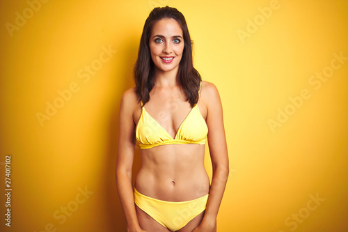 Beautiful woman wearing yellow bikini on summer over isolated yellow background with a happy and cool smile on face. Lucky person.