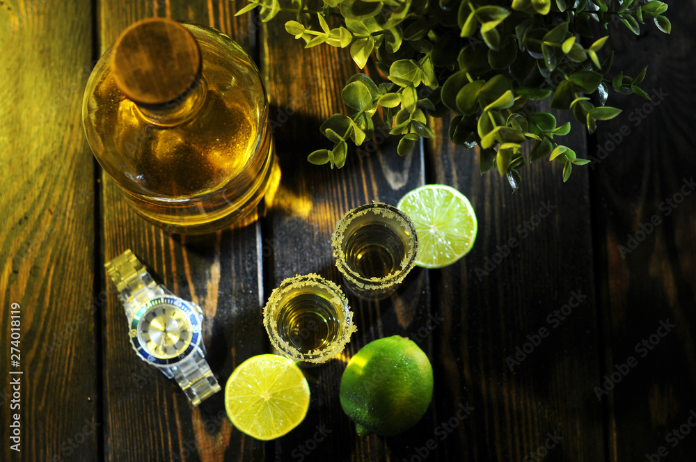 Tequila bottle with fresh lime on a wooden table.Gold Mexican tequila with lime and salt.Studio photography. Tequila bottle with fresh lime on a wooden table.Gold Mexican tequila with lime and salt.Studio photography.