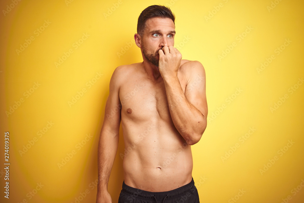 Fototapeta premium Young handsome shirtless man over isolated yellow background looking stressed and nervous with hands on mouth biting nails. Anxiety problem.
