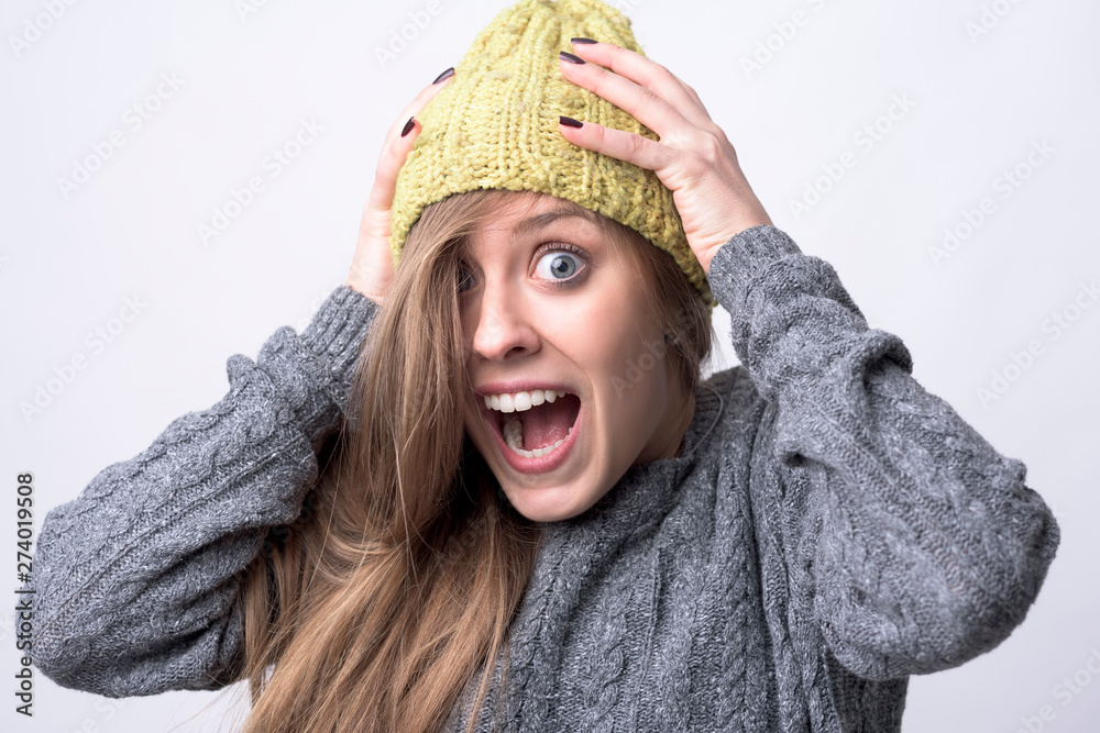 Close up portrait of expressive young woman screaming with hands on head on light gray background. Close up portrait of expressive young woman screaming with hands on head on light gray background.