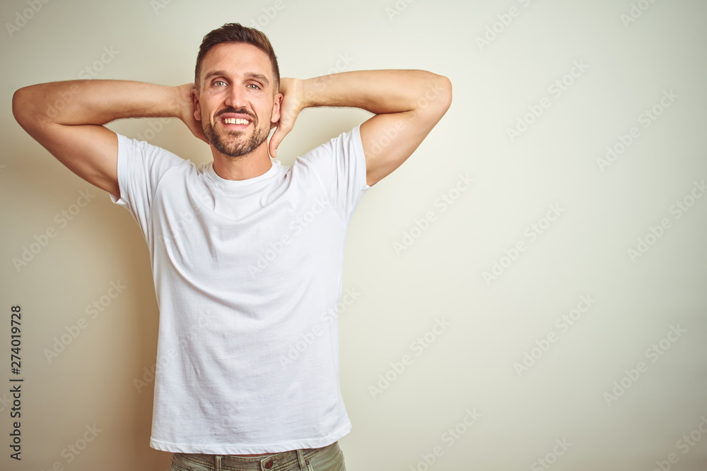 Young handsome man wearing casual white t-shirt over isolated background relaxing and stretching, arms and hands behind head and neck smiling happy Young handsome man wearing casual white t-shirt over isolated background relaxing and stretching, arms and hands behind head and neck smiling happy